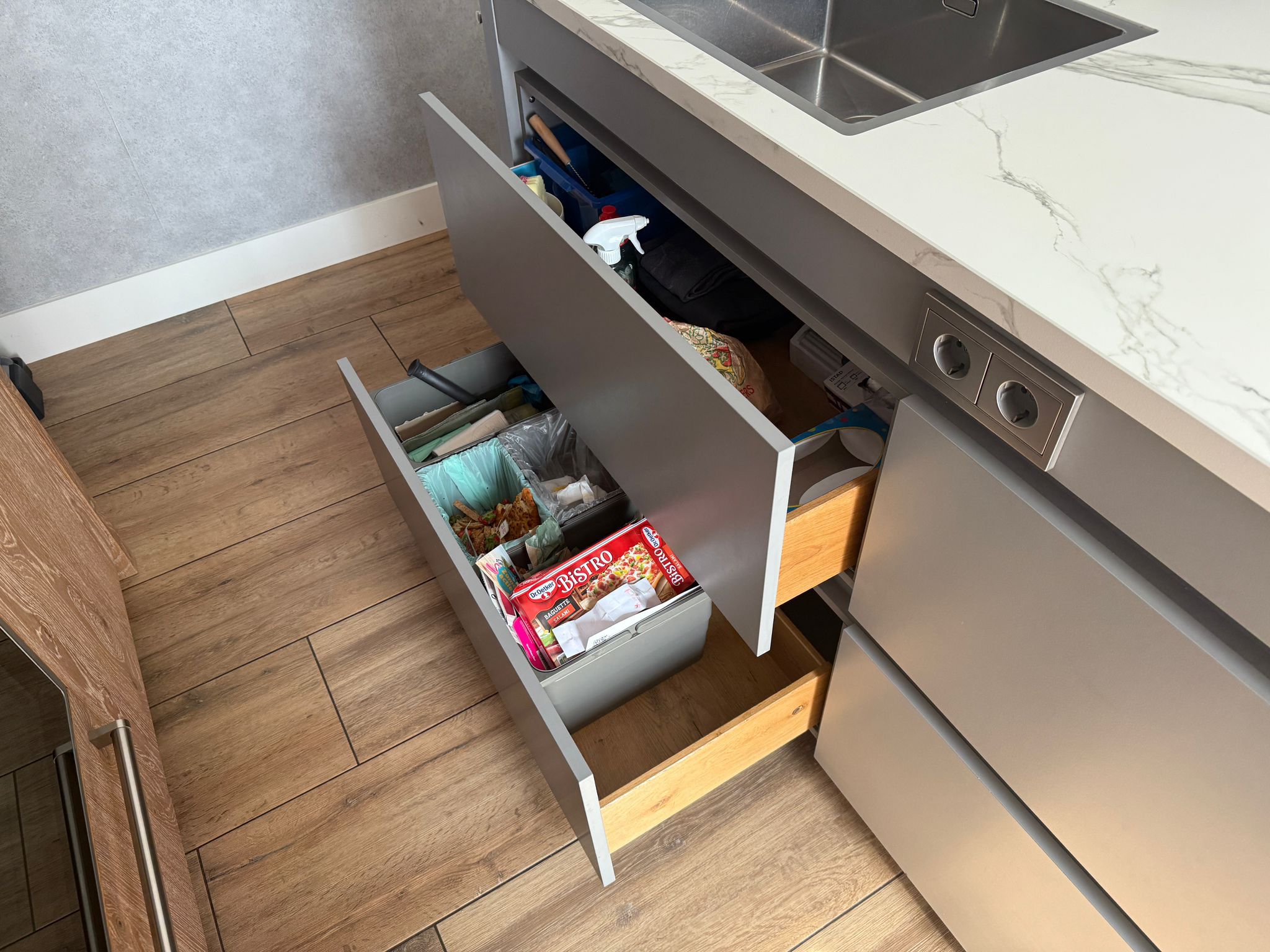 Tweedehandse keuken in houtlook met een grijs kookeiland en kunststoffen blad en openstaande lades met afval
