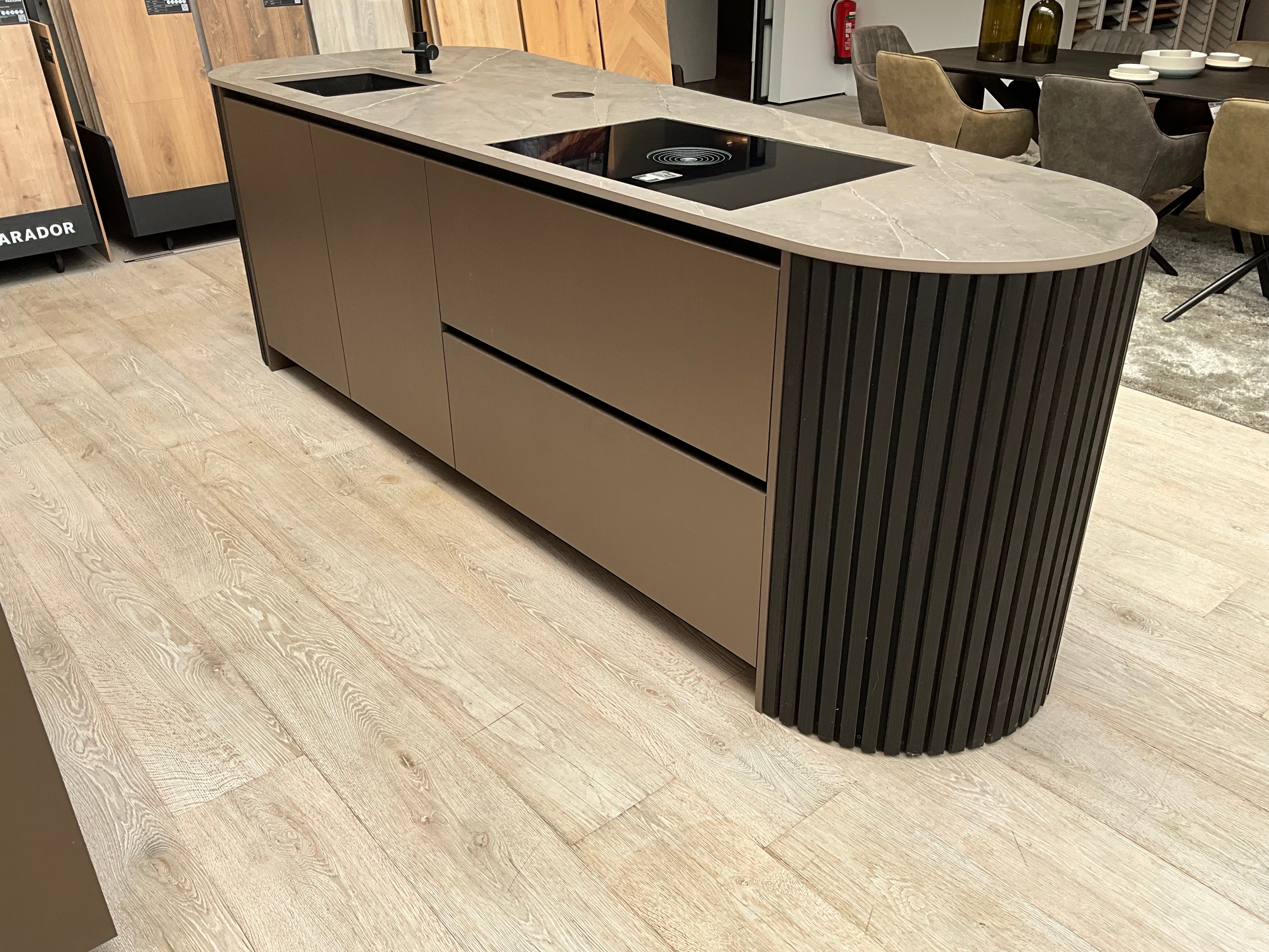 Showroomkeuken van het merk Kembra met kookeiland van zwart hout met champagne bronze kasten met een stenen blad