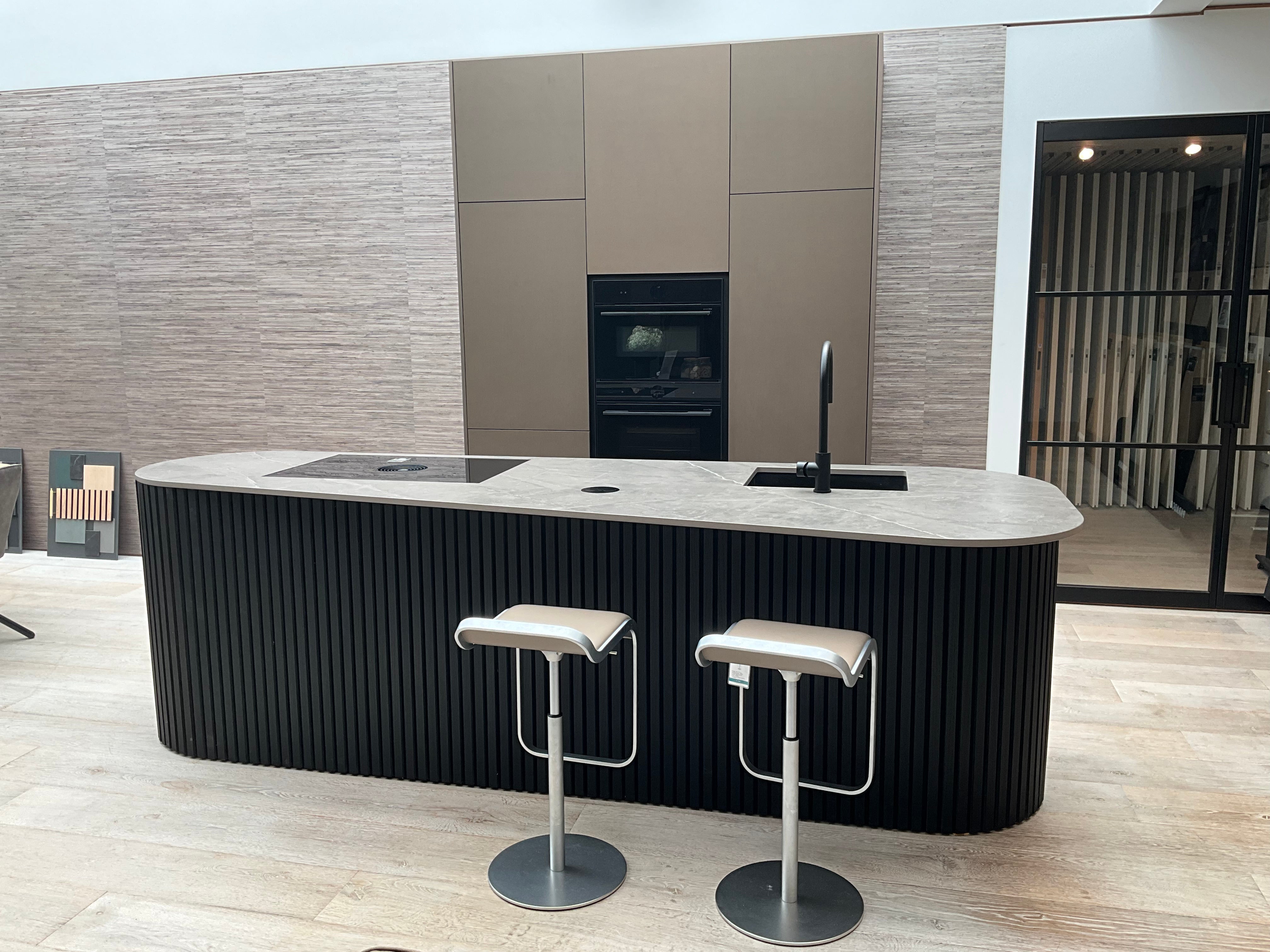 Showroomkeuken van het merk Kembra met kookeiland van zwart hout met champagne brons blad