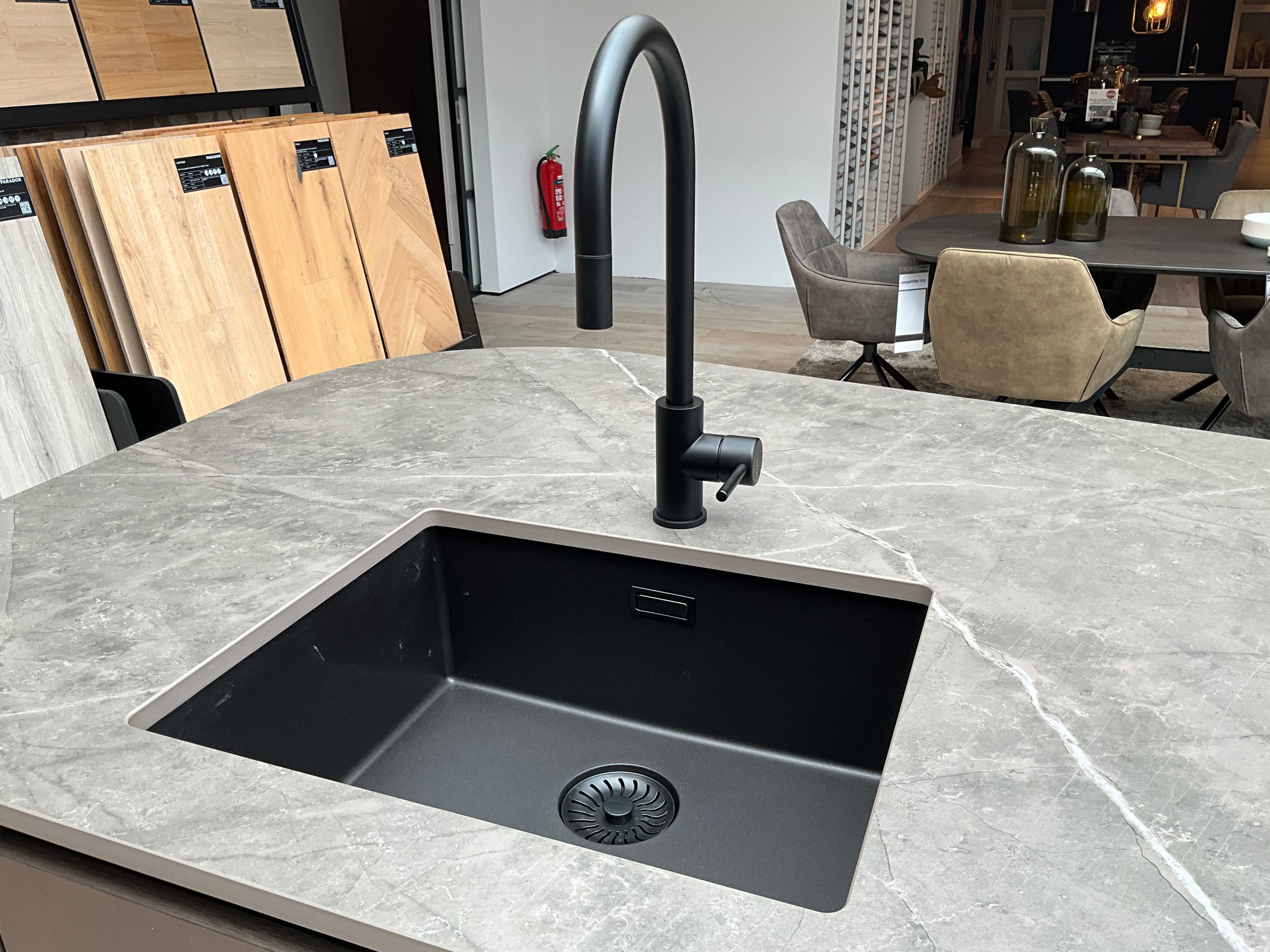 Showroomkeuken van het merk Kembra met kookeiland van zwart hout met champagne brons blad met een zwarte wasbak