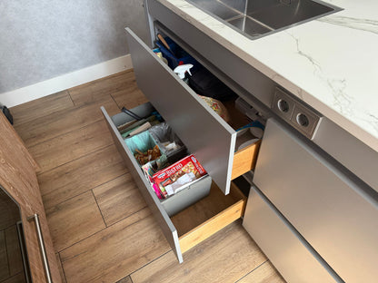 Tweedehandse keuken in houtlook met een grijs kookeiland en kunststoffen blad en openstaande lades met afval