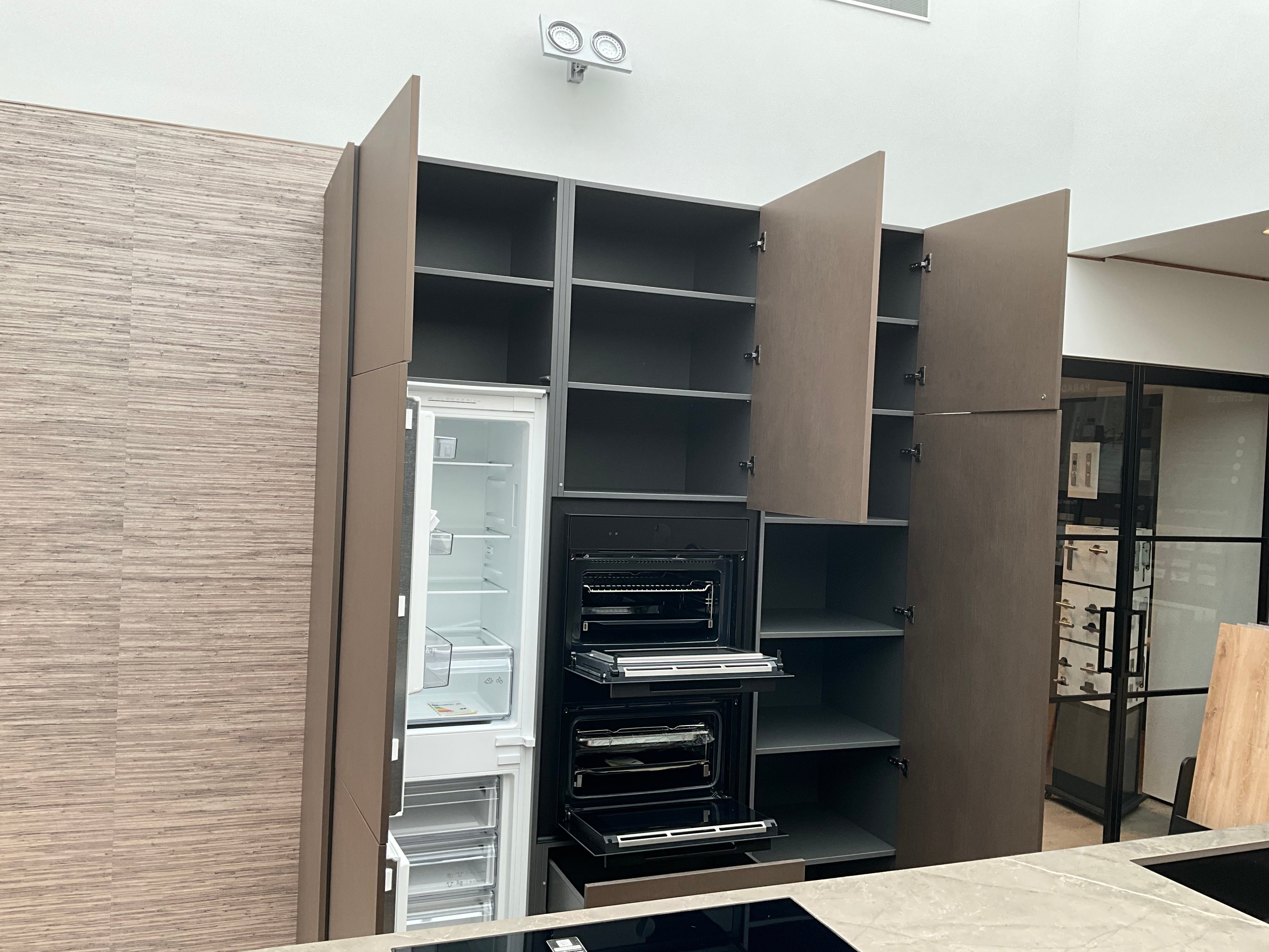 Showroomkeuken van het merk Kembra met kookeiland van zwart hout met champagne bronzen kasten die open staan