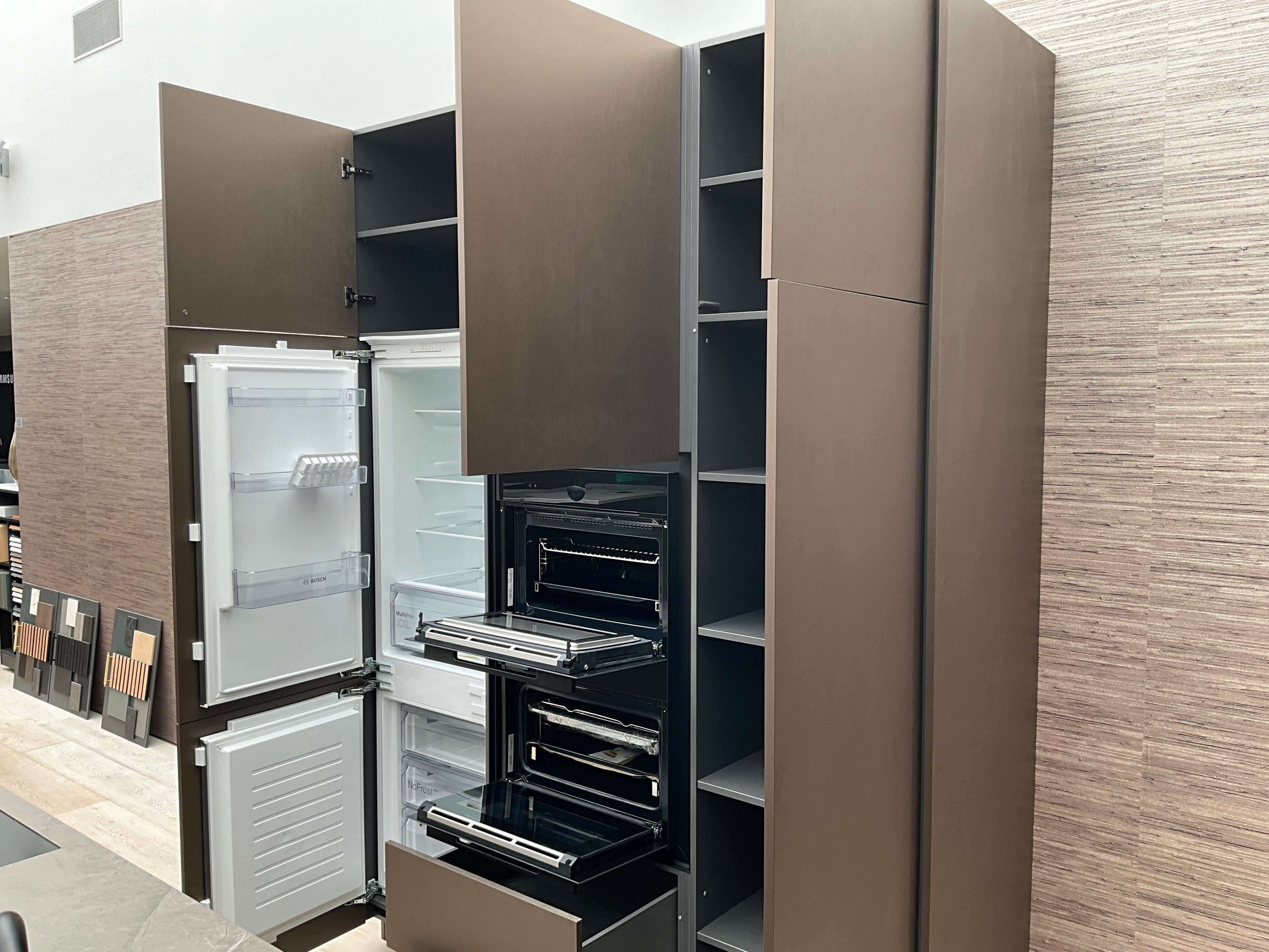 Showroomkeuken van het merk Kembra met kookeiland van zwart hout met champagne bronzen kasten, koelkast en twee ovens